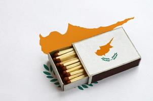 Die zypriotische Flagge wird in einer offenen Streichholzschachtel gezeigt, die mit Streichhölzern gefüllt ist und auf einer großen Flagge liegt foto
