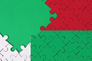 Die Madagaskar-Flagge ist auf einem fertigen Puzzle mit freiem Platz für grüne Kopien auf der linken Seite abgebildet foto
