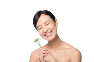 Studioaufnahme einer attraktiven jungen asiatischen Frau mit einem Jade-Roller auf ihrem Gesicht vor einem weißen Hintergrund foto