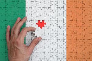 Die irische Flagge ist auf einem Puzzle abgebildet, das die Hand des Mannes zum Falten vervollständigt foto