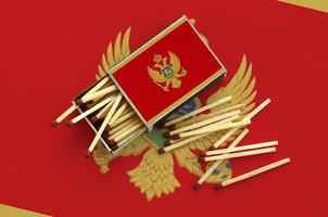 Die montenegro-Flagge wird auf einer offenen Streichholzschachtel gezeigt, aus der mehrere Streichhölzer fallen und auf einer großen Fahne liegt foto
