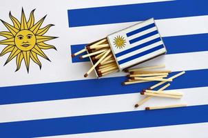 die uruguay-flagge ist auf einer offenen streichholzschachtel abgebildet, aus der mehrere streichhölzer fallen und die auf einer großen fahne liegt foto