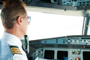 bereiten sich auf den Flug vor. Rückansicht des selbstbewussten männlichen Piloten, der im Flugzeugcockpit sitzt foto