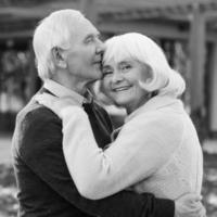 Porträt endloser Liebe. Schwarz-Weiß-Porträt eines glücklichen Seniorenpaares, das sich aneinander bindet und lächelt, während es im Freien und vor ihrem Haus steht foto