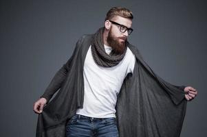 sieht cool und trendy aus. hübscher junger bärtiger mann mit brille, der vor grauem hintergrund posiert foto