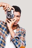 Gib mir ein Lächeln hübscher junger afroamerikanischer Mann, der ein Foto macht und lächelt, während er vor grauem Hintergrund steht