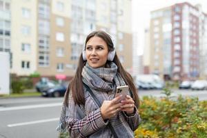 Junge stilvolle Frau, die mit Kopfhörern die Straße hinuntergeht und Musik vom Telefon hört foto