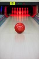 Moment, wenn das Herz aufhört zu schlagen. Nahaufnahme der leuchtend roten Bowlingkugel, die entlang der Bowlingbahn rollt foto