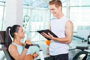 Planung ihres Tages im Fitnessstudio. schöne junge sportliche frau, die mit ihrem sportlehrer spricht und lächelt foto