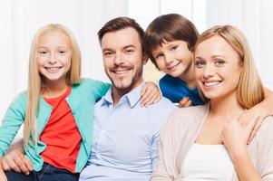 glücklich, eine Familie zu sein. glückliche vierköpfige Familie, die sich aneinander bindet und lächelt, während sie drinnen sitzt foto