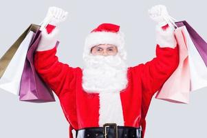 weihnachtsverkäufe glücklicher weihnachtsmann, der einkaufstüten hält, während er gegen grauen hintergrund steht foto