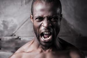 wütend und aggressiv. Porträt eines wütenden jungen, hemdlosen Afrikaners, der schreit und in die Kamera schaut foto