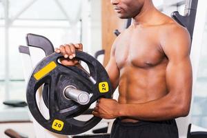 Vorbereitung auf das Training. Nahaufnahme eines muskulösen afrikanischen Mannes, der sich auf das Gewichtheben vorbereitet, während er im Fitnessstudio steht foto