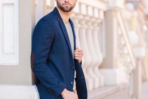 in seinem eigenen perfekten Stil. Zugeschnittenes Bild eines gutaussehenden jungen Mannes mit Brille und eleganter Jacke, der wegschaut, während er im Freien steht foto