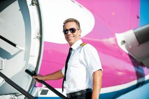 ich bin bereit zu fliegen selbstbewusster männlicher pilot in uniform, der in das flugzeug geht und lächelt foto