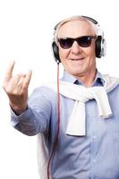 Rockstar. Fröhlicher älterer Mann mit Kopfhörern, der Musik hört und Handzeichen zeigt, während er vor weißem Hintergrund steht foto