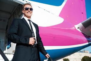 gerade angekommen. Tiefwinkelansicht eines selbstbewussten, reifen Geschäftsmanns, der aus dem Flugzeug steigt und lächelt foto