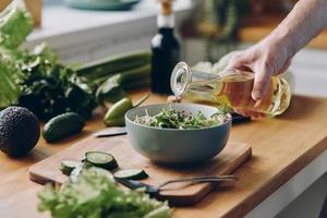 Nahaufnahme eines nicht erkennbaren Mannes, der Olivenöl mit frischem Salat in die Schüssel gießt foto