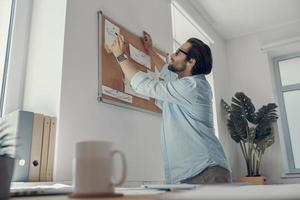 Selbstbewusster junger Mann, der sich während der Arbeit im Büro Notizen macht foto