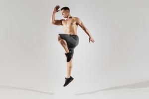 Selbstbewusster junger Mann mit perfektem Körper, der vor weißem Hintergrund springt foto