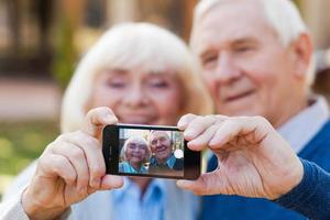 Einfangen der endlosen Liebe. glückliches älteres paar, das sich aneinander bindet und selfie macht, während es im freien steht foto