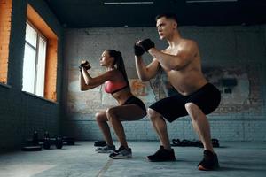 selbstbewusstes, fittes Paar, das in der Hocke steht, während es gemeinsam im Fitnessstudio trainiert foto