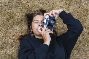 süßes jugendlich Mädchen mit einer Kamera, ein Mädchen, das Fotos auf einer Retro-Vintage-Kamera auf dem Gras im Park macht, ein Hobbykonzept