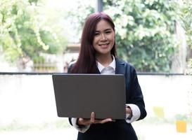 attraktive junge asiatische frau, die laptop-computer verwendet, während sie in einem büro steht. foto