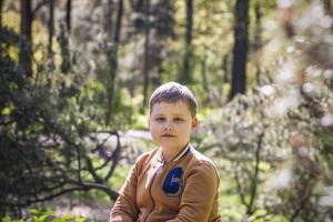 ein süßer junger mann sitzt und posiert auf einer lichtung im wald. Die Sonnenstrahlen umhüllen den Raum der Lichtung mit einem Baumstumpf. Platz zum Kopieren. foto