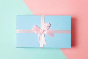 kleine geschenkbox verpackt blaues papier isoliert auf blauem und rosa pastellfarbenem trendigen geometrischen hintergrund. weihnachten neujahr geburtstag valentinstag feier vorhanden romantisches konzept. foto
