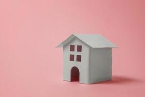einfach design mit miniatur-weißem spielzeughaus isoliert auf rosa pastellfarbenem trendigem hintergrund. Hypotheken-Sachversicherung Traumhaus-Konzept. Platz kopieren. foto