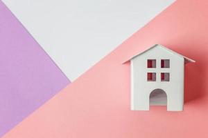 einfach design mit miniatur-weißem spielzeughaus isoliert auf weißem violett-rosa pastellfarbenem trendigen geometrischen hintergrund. Hypotheken-Sachversicherung Traumhaus-Konzept. flach liegend draufsicht kopierraum. foto