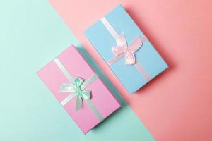 kleine geschenkbox verpackt in rosa und blauem papier isoliert auf blauem und rosa pastellfarbenem, trendigem geometrischem hintergrund. weihnachten neujahr geburtstag valentinstag feier vorhanden romantisches konzept. foto