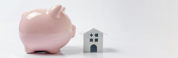Design einfach mit weißem Miniaturspielzeughaus, rosa Sparschwein isoliert auf weißem Hintergrund. Hypotheken-Sachversicherung Traum-Home-Banking-Investitionsdarlehenskonzept. kopierraum, banner.