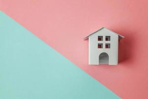 einfach design mit miniatur-weißem spielzeughaus isoliert auf blau-rosa pastellfarbenem, trendigem geometrischem hintergrund. Hypotheken-Sachversicherung Traumhaus-Konzept. flach liegend draufsicht kopierraum. foto