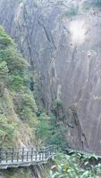 Die wunderschönen Berglandschaften mit dem grünen Wald und einer Plankenstraße, die entlang einer Klippe in der Landschaft Chinas gebaut wurde foto