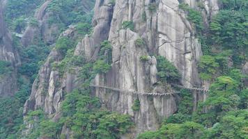 Die wunderschönen Berglandschaften mit dem grünen Wald und einer Plankenstraße, die entlang einer Klippe in der Landschaft Chinas gebaut wurde foto