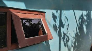 braunes Fenster an blauer Wand mit Schatten der Blätter 2 foto