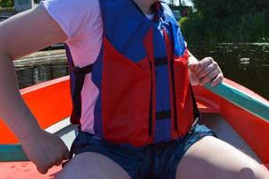 ein mann in einem roten boot, shorts und einer schwimmweste paddelt mit rudern auf einem boot für einen spaziergang auf dem wasser des seeflussmeeres in der natur foto