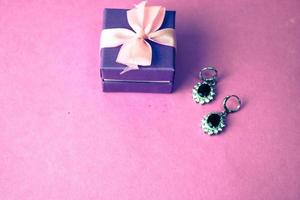 Schönheitsbox, festliche schöne Geschenkbox mit einer Schleife mit silbernen Ohrringen mit Edelsteinen auf einem rosa lila Hintergrund. flach liegen. Ansicht von oben foto