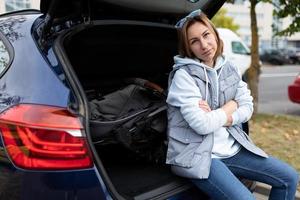 eine junge frau sitzt im kofferraum, der einen kinderwagen lädt und sich ausruht, alleinerziehendes mutterkonzept foto