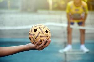 Sepak-Takraw-Ball, traditioneller Sport der südostasiatischen Länder, der eine junge asiatische Sepak-Takraw-Spielerin vor dem Netz in der Hand hält, bevor sie sie einem anderen Spieler zuwirft, um über das Netz zu treten. foto
