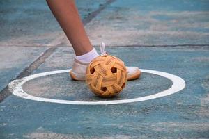 Sepak-Takraw-Ball, traditioneller Sport der südostasiatischen Länder, der eine junge asiatische Sepak-Takraw-Spielerin vor dem Netz in der Hand hält, bevor sie sie einem anderen Spieler zuwirft, um über das Netz zu treten. foto