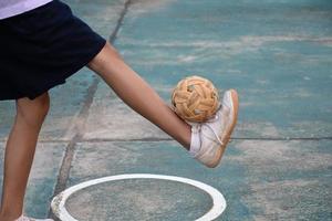 Sepak-Takraw-Ball, traditioneller Sport der südostasiatischen Länder, der eine junge asiatische Sepak-Takraw-Spielerin vor dem Netz in der Hand hält, bevor sie sie einem anderen Spieler zuwirft, um über das Netz zu treten. foto