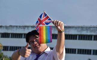 asiatischer junge hält regenbogenflagge und union jack-flagge und trägt krawatte und steht außerhalb des gebäudes, weicher und selektiver fokus, konzept für lgbtq-feier im stolzmonat. foto