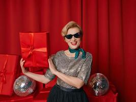 schöne, stilvolle, reife Frau mit Sonnenbrille im Einkaufswagen auf Geschenkboxen-Hintergrund. party, feier, einkaufen, konsumkonzept foto