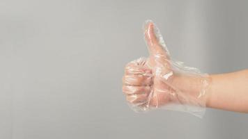 Die Hand trägt einen Einweg-Plastikhandschuh und mag ein Handzeichen auf grauem Hintergrund. foto