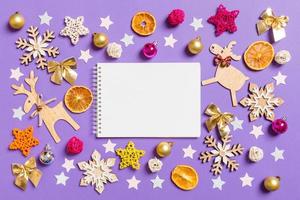 Blick von oben auf das Notizbuch, umgeben von Spielzeug und Dekorationen des neuen Jahres auf violettem Hintergrund. Weihnachtszeit-Konzept foto