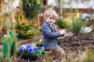 kleiner Junge, der im Garten arbeitet und Blumen pflanzt