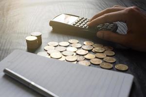 Nahaufnahme der Hand des Mannes mit Taschenrechner mit Goldmünzen, Stift, Notizbuch auf schwarzem Tisch. Business, Finanzen, Marketing, E-Commerce-Konzept und Design foto